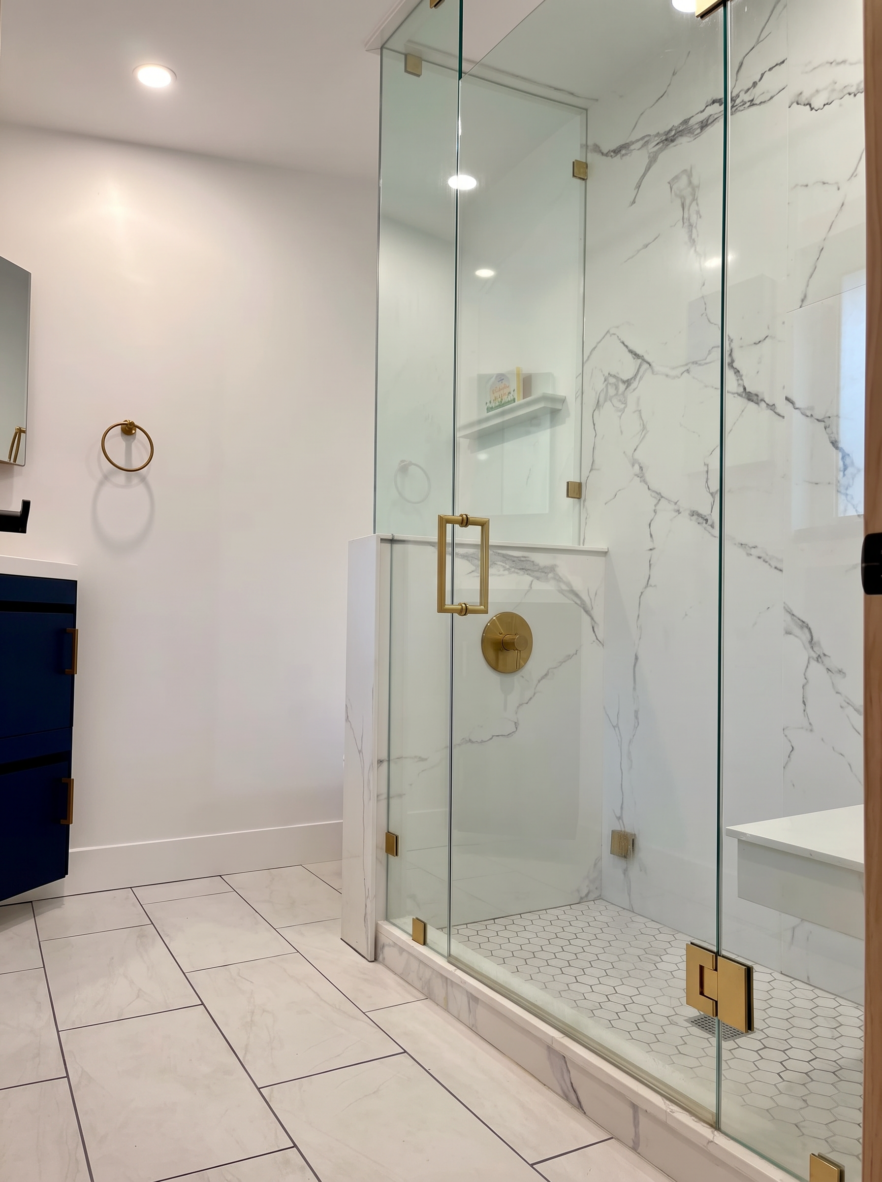ADU spa bath with Mr. Steam steam shower, large-format marble-look panels, brass fixtures, and navy vanity